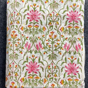 Könnte beinhalten: Gefalteter weißer Stoff mit einem sich wiederholenden Blumenmuster. Große rosa Lotusblüten sind mit kleineren gelben und roten Blüten, grünen Blättern und rosa Vögeln durchsetzt. Der Stoff ist wahrscheinlich Baumwolle oder Leinen.