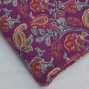 May include: A folded piece of fabric with a vibrant floral pattern. The design features paisley and flower motifs in shades of orange, red, and pink against a deep purple background. Gray-green leaves and stems complete the design.
