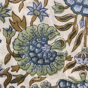 May include: Close-up of a fabric with a floral pattern. The design features large, stylized flowers in shades of blue and green, with brown stems and leaves, set against a cream-colored background. The fabric has a textured appearance.