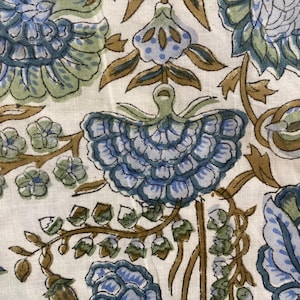 May include: Close-up of a fabric with a floral pattern. The design features large blue and green flowers with brown stems and leaves against a white background. The fabric has a vintage or bohemian aesthetic.