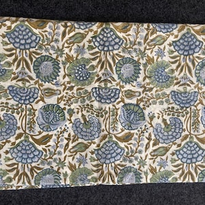 May include: A folded piece of fabric with a repeating floral pattern. The design features stylized blue and green flowers, brown stems, and small leaves on an off-white background. The fabric is likely cotton or linen.