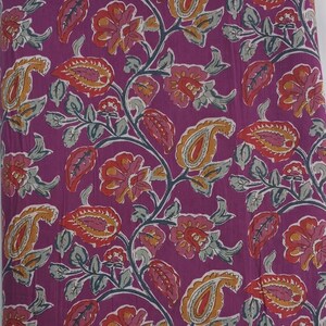 May include: A fabric with a repeating floral pattern in shades of purple, red, orange, and yellow. The design includes paisley shapes, flowers, and leaves on a purple background. The fabric is likely cotton or a similar material.