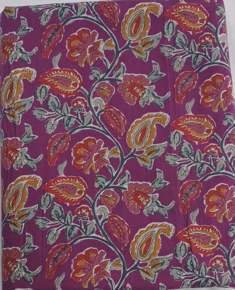 May include: A fabric with a repeating floral pattern in shades of purple, red, orange, and yellow. The design includes paisley shapes, flowers, and leaves on a purple background. The fabric is likely cotton or a similar material.
