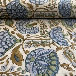 May include: Close-up of a fabric with a repeating floral pattern. The design features large, stylized blue flowers with green accents and brown stems and leaves, set against a cream background. The fabric is folded over.
