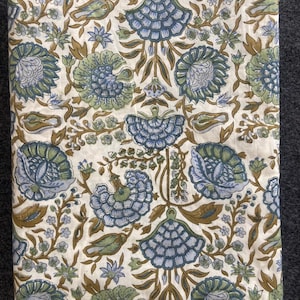 May include: A folded fabric with a repeating floral pattern. The design features large, stylized blue and green flowers with brown stems and leaves on a white background. The fabric is likely cotton or linen.