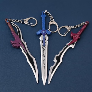 Puede incluir: Tres llaveros de espada de fantasía con hojas plateadas, detalles en negro y empuñaduras coloridas en morado, rojo y azul. Cada llavero tiene una cadena y un cierre plateados. Las espadas se muestran sobre una superficie azul.