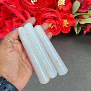 Puede incluir: Cuatro varitas de cristal cil&iacute;ndricas blancas con un sutil patr&oacute;n natural. Las varitas se sostienen en una mano, con rosas rojas en el fondo. Las varitas son lisas y pulidas.