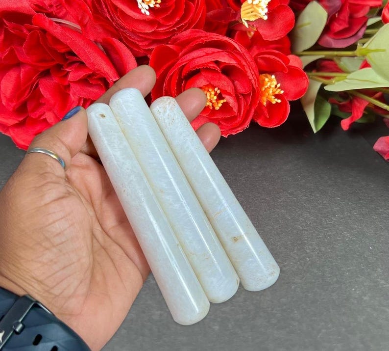 Puede incluir: Cuatro varitas de cristal cil&iacute;ndricas blancas con un sutil patr&oacute;n natural. Las varitas se sostienen en una mano, con rosas rojas en el fondo. Las varitas son lisas y pulidas.