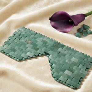 Può includere: Una maschera per occhi in giada verde composta da piccole tessere rettangolari in pietra intrecciate insieme con un bordo di perline. La maschera presenta una forma sagomata con due sezioni distinte per gli occhi e un ponte nasale.