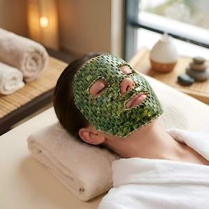 Op de afbeelding: Een gezichtsmasker opgebouwd uit kleine, vierkante, gepolijste groene jadetegels die in een rasterpatroon met elkaar zijn verbonden. Het masker bedekt het voorhoofd, de wangen, de neus en de kin, met uitsparingen voor de ogen, neusgaten en mond.