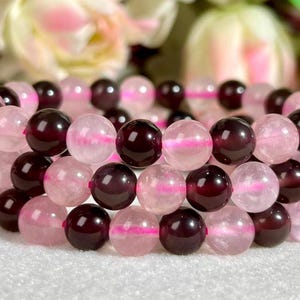 May include: A multi-strand beaded bracelet featuring alternating round polished beads in deep dark red garnet and translucent pale pink rose quartz. The beads are strung together on a flexible cord, creating a layered circular design with a smooth finish.
