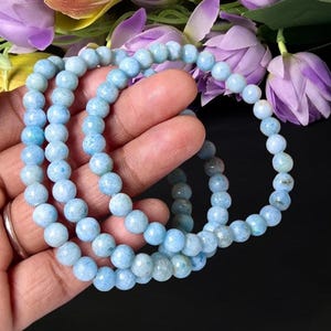May include: A stretch bracelet composed of round, light blue gemstone beads with subtle internal variations. The beads are strung together in a continuous loop, displaying a smooth, polished finish and a consistent pale sky blue color throughout.