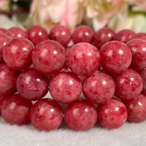 Peut inclure: Un bracelet multi-rangs composé de perles sphériques polies dans des nuances variées de rose foncé et de magenta. Les perles présentent des motifs naturels marbrés et une finition lisse et brillante, disposées en plusieurs rangées.