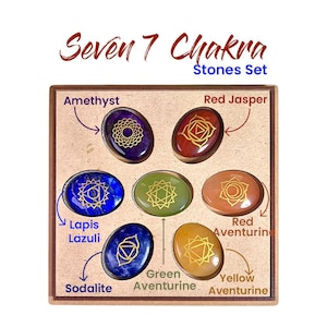May include: A set of seven chakra stones in a wooden box. Each oval stone is a different color, including purple, red, blue, green, and orange. Each stone has a gold-colored symbol. The text "Seven 7 Chakra Stones Set" is at the top.