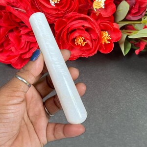 Puede incluir: Un objeto cil&iacute;ndrico blanco y c&oacute;nico con una superficie texturizada. El objeto se sostiene en una mano, con rosas rojas en el fondo. El objeto parece estar hecho de piedra o un material similar.