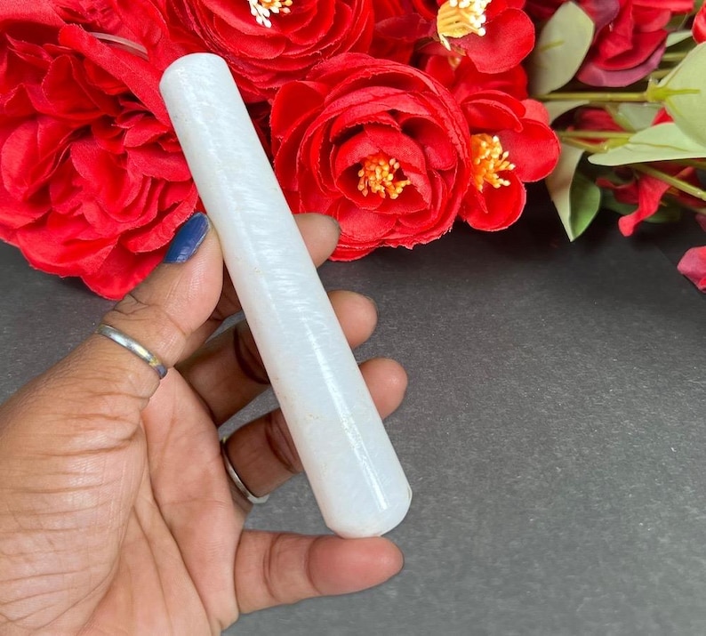 Puede incluir: Un objeto cil&iacute;ndrico blanco y c&oacute;nico con una superficie texturizada. El objeto se sostiene en una mano, con rosas rojas en el fondo. El objeto parece estar hecho de piedra o un material similar.