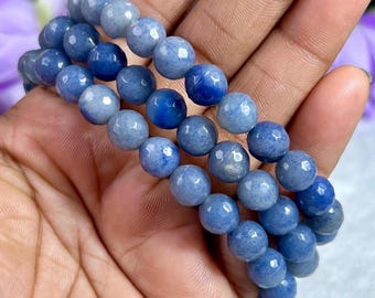 May include: Three blue beaded bracelets with varying shades of blue. The beads are round and appear to be made of a polished stone. The bracelets are stacked on top of each other.