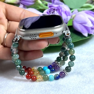 May include: Silver smartwatch with a multi-coloured beaded strap. The strap incorporates a rainbow of gemstones, including red, orange, yellow, green, blue, and purple. The watch has a black screen and an orange accent.