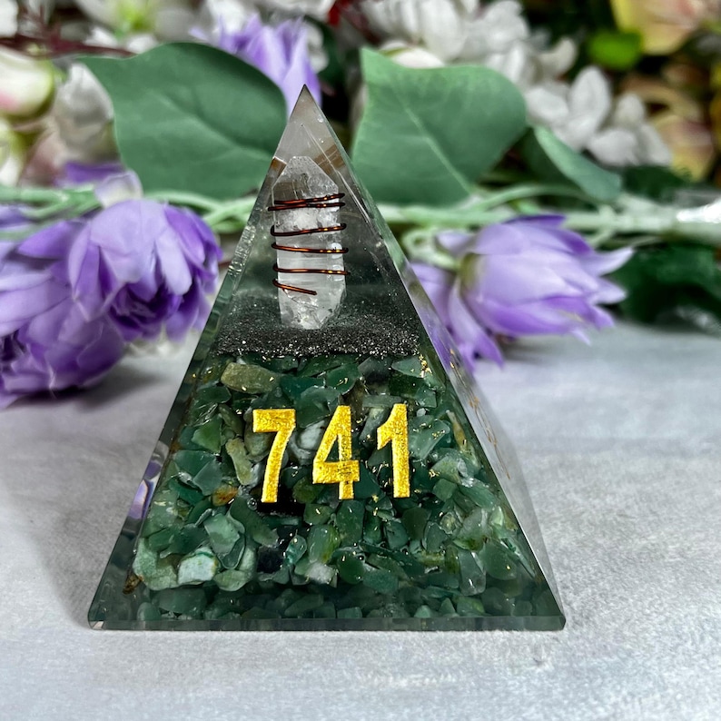 May include: A pyramid-shaped decorative object with a clear top, green base, and the number 741 in gold. A clear crystal is wrapped in copper wire and is visible inside the pyramid. The base is filled with green stones.