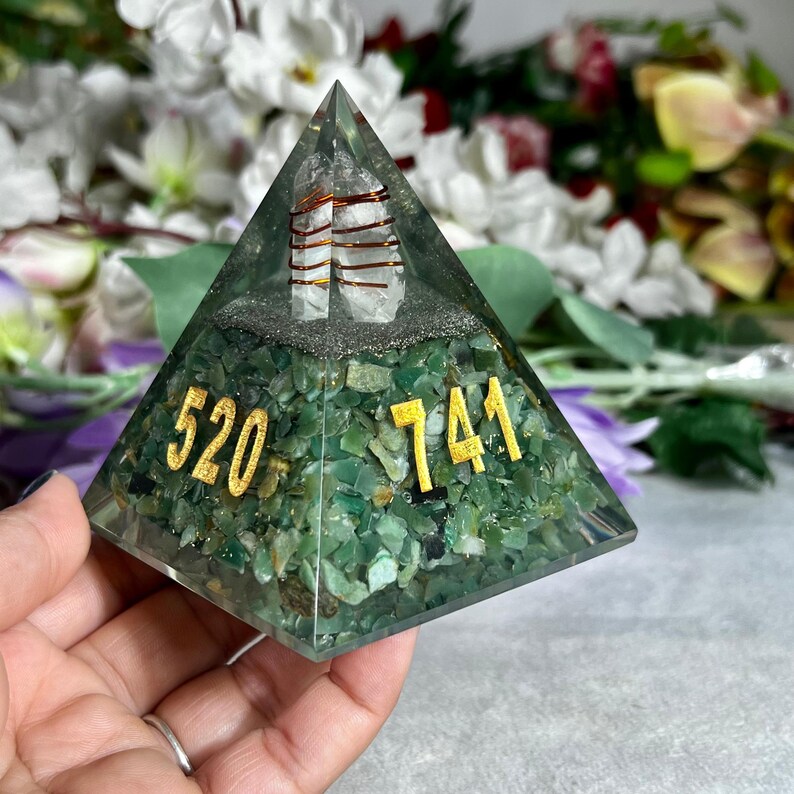 May include: A green pyramid-shaped resin art piece with embedded green stones and gold numbers. The pyramid has a clear top with two clear quartz crystals wrapped in copper wire. The numbers "520" and "741" are displayed in gold.