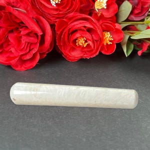 Puede incluir: Un objeto cil&iacute;ndrico de color claro con extremos redondeados. El objeto tiene una apariencia veteada y est&aacute; colocado sobre un fondo oscuro con flores rojas.