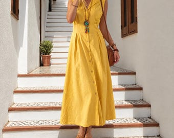 May include: A sleeveless, ankle-length yellow button-down dress with a collared neckline and a pleated waist. The dress features a row of buttons running down the center front and is paired with brown strappy sandals and a long beaded pendant necklace.