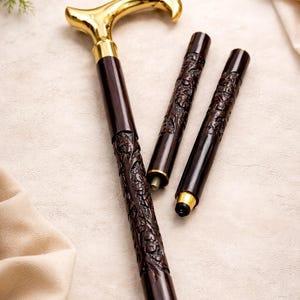 May include: A collapsible walking cane featuring a polished gold-tone handle and a dark brown shaft. The shaft is composed of three segments, with two sections displaying intricate carved floral patterns and gold-tone metal connectors.