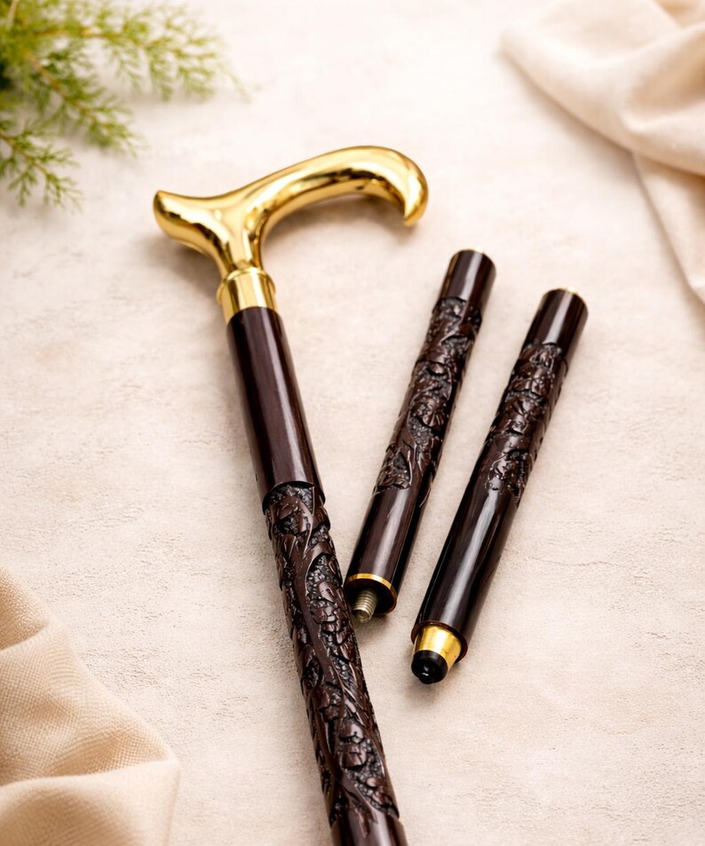 May include: A collapsible walking cane featuring a polished gold-tone derby handle and a dark brown shaft with intricate floral carvings. The cane is shown in three segments, with threaded metal connectors visible for assembly and a black rubber tip.