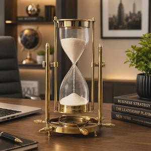 May include: A brass hourglass with a rotating frame and a compass integrated into the circular base. The hourglass contains white sand flowing between two clear glass bulbs. The structure features vertical supports and decorative pointed accents.