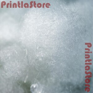 The image is a close-up of a fluffy, white material, possibly cotton or a similar soft fiber.