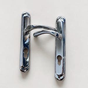 May include: A pair of polished chrome door handles with long, vertical rectangular backplates. Each backplate features a rounded top and bottom with a keyhole cutout at the base. The curved, ergonomic lever handles are attached to the center plates.