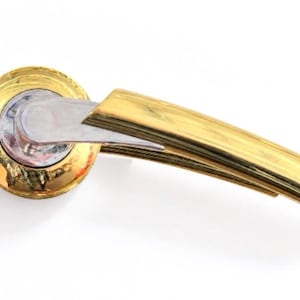 Peut inclure: Une poignée de porte dotée d'un levier incurvé en finition dorée polie, fixée sur une base circulaire. La base présente un anneau extérieur doré entourant un élément central argenté. Le levier s'étend avec une finition métallique lisse.