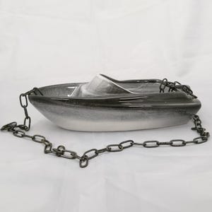 May include: A ceramic boat-shaped planter featuring a glossy gradient finish that transitions from dark charcoal at the top to a light grey at the base. The vessel is suspended by a dark metal chain attached to the bow and stern sections.