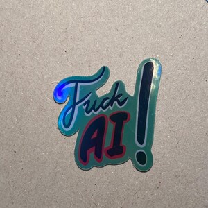 May include: A teal sticker with the words "Fuck AI" in a stylized font. The word "Fuck" is in teal with a white outline, and "AI" is in red with a white outline. A black exclamation point is next to the words.