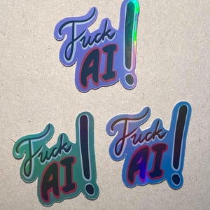 May include: Three holographic stickers with the text "Fuck AI" in a stylized font. The stickers have a gradient of colors, including blue, green, and pink, with a shiny, reflective finish. Each sticker features an exclamation point.