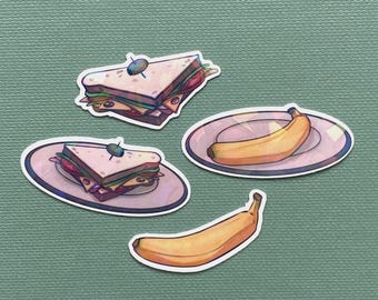 以下が含まれることがあります： 緑色の背景に4つの食品ステッカー。2つのステッカーは爪楊枝付きのサンドイッチを示し、2つのステッカーはバナナを示し、1つはお皿に乗っています。サンドイッチには食材が層になっています。バナナは黄色です。