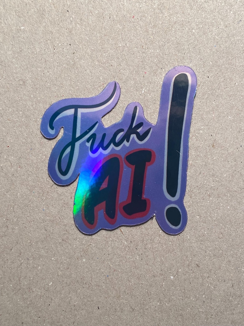 May include: A purple sticker with the words "Fuck AI" in a stylized font. The sticker has a holographic effect and a black exclamation point. The letters "AI" are in red.