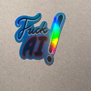 May include: A holographic sticker with the words "Fuck AI!" in a stylized font. The sticker has a blue border and a rainbow-colored exclamation point. The text "AI" is in red.
