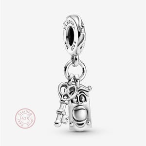 May include: A silver charm depicting a key and a door with a face. The charm hangs from a larger silver bead, engraved with "Pandora". The charm is marked "Sterling 925". A small, round stamp reads "Real Silver".