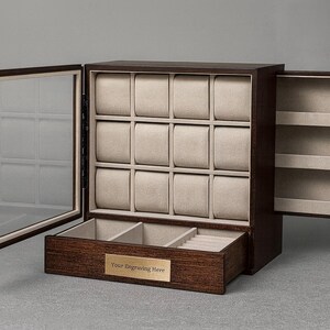 K&ouml;nnte beinhalten: Eine dunkelbraune Uhrenvitrine aus Holz mit Glast&uuml;r und Schublade. Der Innenraum hat beige Kissen f&uuml;r Uhren und Regale an der T&uuml;r. Die Schublade hat F&auml;cher. Der Text "Your Engraving Here" befindet sich auf einem goldenen Schild.