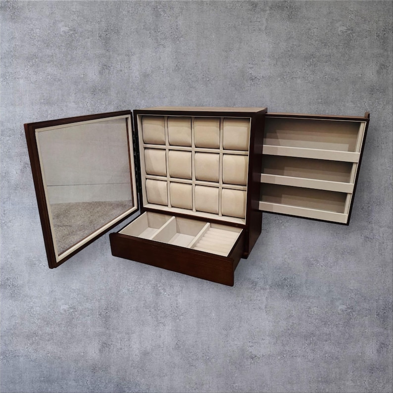 K&ouml;nnte beinhalten: Eine dunkelbraune Holz-Uhrenbox mit Spiegel, mehreren Uhrenf&auml;chern und einer Schublade. Der Innenraum verf&uuml;gt &uuml;ber beige Kissen f&uuml;r Uhren und ein beiges Futter. Die Box ist ge&ouml;ffnet und zeigt ihren Inhalt und ihr Design.