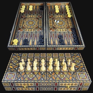 Op de afbeelding: Een houten backgammon- en schaakbordset met ingewikkeld geometrisch inlegwerk in tinten bruin, geel en zwart. Het open bord toont backgammonpunten met gele en zwarte schijven en dobbelstenen, terwijl de gesloten kant schaakstukken laat zien.
