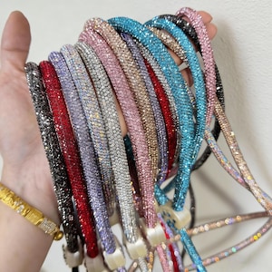Puede incluir: Una colección de correas de teléfono coloridas y brillantes. Las correas están cubiertas de pequeños pedrería reflectante en varios colores, incluyendo negro, rojo, plateado, rosa y azul. Cada correa tiene aproximadamente 1,3 cm de diámetro.