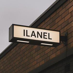 Może przedstawiać: Prostokątny, podświetlany szyld z napisem "ILANEL" pogrubionymi, czarnymi literami. Szyld jest zamontowany na ceglanej ścianie i posiada dwa poziome światła. Tło szyldu jest w jasnobeżowym kolorze.