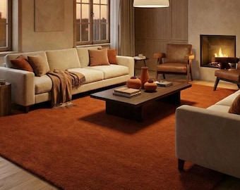 May include: A cozy living room with a large, rust-colored rug. Two cream-colored sofas are adorned with brown pillows and a matching throw. A dark wood coffee table holds decorative vases. A fireplace and large windows complete the warm, inviting space.