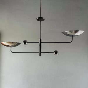Puede incluir: Lámpara colgante moderna de metal negro con dos pantallas plateadas en forma de cuenco y dos acentos esféricos. La lámpara cuelga de una varilla central y presenta un diseño minimalista. Adecuada para un comedor o sala de estar.