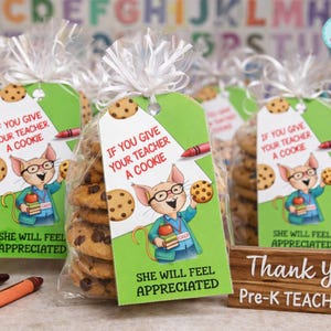 May include: Clear cellophane bags filled with chocolate chip cookies, tied with white ribbon. Each bag has a green tag with a cartoon mouse holding cookies and the text "If You Give Your Teacher A Cookie". A wooden sign reads "Thank You Pre-K Teachers".