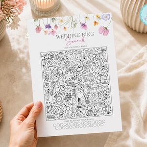 May include: A white paper activity sheet titled WEDDING RING SEARCH with a floral border. The center features a black and white line art puzzle containing various wedding-themed illustrations and a row of twenty-seven empty circles at the bottom.
