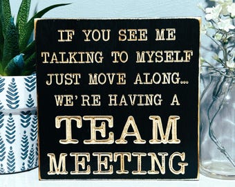 May include: Black wooden sign with gold lettering that reads "If you see me talking to myself just move along... We're having a team meeting."