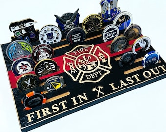 Puede incluir: Un expositor de monedas de madera negra con una franja roja y blanca y un emblema de bombero dorado. El emblema tiene las palabras "FIRE DEPT" y una escalera y un casco de bombero. El expositor tiene 24 ranuras para monedas y las palabras "FIRST IN LAST OUT" están impresas en la parte inferior.